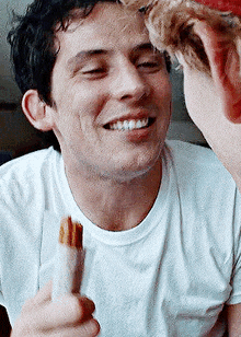 a man in a white shirt is smiling while holding a piece of food in his hand