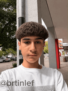 a young man with curly hair is wearing a white shirt that says @brtinlef on it