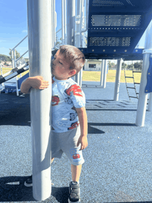 a young boy wearing a lightning mcqueen shirt leans on a pole in a playground