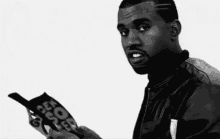 kanye west is smoking a cigarette while holding a cell phone .