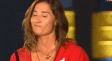 a woman in a red shirt and necklace is making a funny face with her eyes closed .