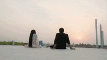 a man and a woman sit on a roof looking at the sun