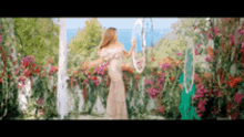 a woman in a long white dress is holding a hula hoop in a garden .