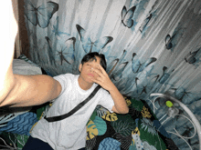a young man taking a selfie in front of a blue butterfly curtain