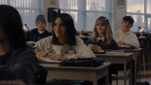 a girl wearing a sweatshirt that says ' a ' on it sits in a classroom with other students