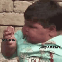 a baby is eating a piece of food with the words major academy written on it .