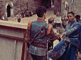 a woman in a blue dress holds the hand of a man in a blue jacket