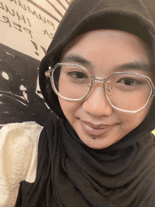 a woman wearing glasses and a hijab smiles for a photo