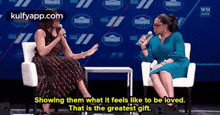 two women are sitting in chairs talking to each other while one of them is holding a microphone .