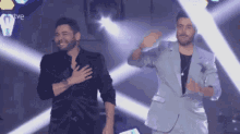 two men are standing on a stage with their hands on their chests and the word tve on the bottom