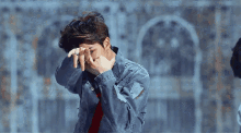 a man wearing a denim jacket covering his face with his hands