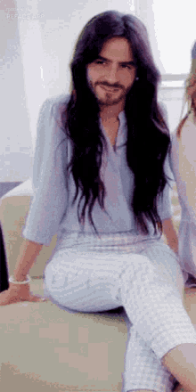 a man with long hair and a beard is sitting on a couch .