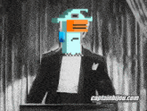 a man in a tuxedo stands at a podium with captainbijou.com written on the bottom right