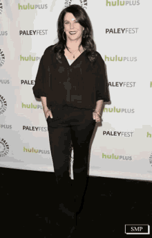 a woman in a black shirt and black pants is standing in front of a wall that says hulu plus