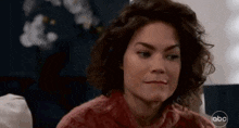a woman with curly hair is wearing a pink sweater and making a funny face .