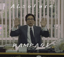 a man in a suit and tie sits at a desk with his hands in the air and the words absolute rampage written above him