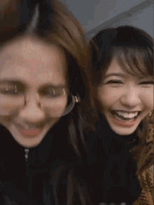 two young women are standing next to each other and smiling . one of the girls is wearing glasses .