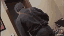 a man in a black jacket and hat is standing in a doorway in a room .