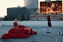 a woman in a red dress sits on a bed in front of a billboard that says " dont clock "