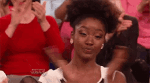 a woman is sitting in a crowd of people clapping and making a face .