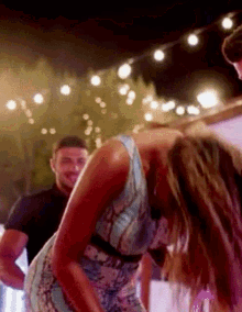 a woman in a blue dress is bending over in front of a man in a black shirt