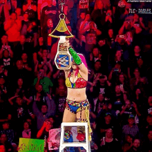 a woman with pink and blue hair is sitting on a ladder holding a wrestling championship belt