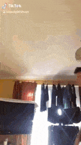 a man is standing in front of a window in a room with clothes hanging on a rack .