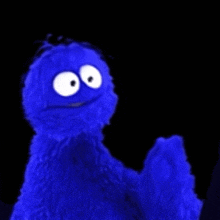 a blue sesame street cookie monster with white eyes is standing in the dark