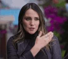 a woman wearing a black turtleneck and a leather jacket is clapping her hands