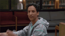 a man in a gray hoodie is sitting at a table in a waiting room .