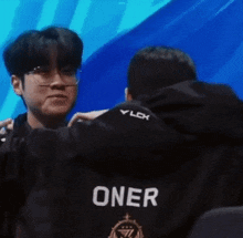 a man wearing a black jacket with the name oner on the back is hugging another man