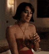 a woman in a red dress is sitting on a bed holding a wine glass .