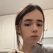 a young woman is making a funny face in front of a kitchen cabinet .