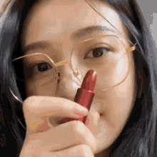 a woman wearing glasses holds a red lipstick in her hand