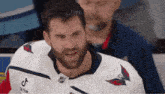 a man with a beard is wearing a white hockey jersey and smiling .