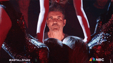 a man stands in front of a group of dancers with a nbc logo in the corner