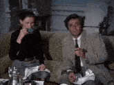 a man and woman are sitting on a couch drinking tea