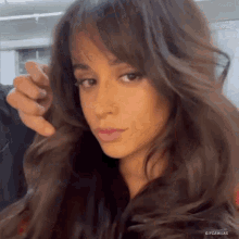 a close up of a woman 's face with long hair and a hand holding her hair .