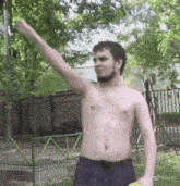 a shirtless man is holding a tennis ball in a park