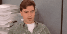 a man wearing a green paisley shirt is sitting in front of a stack of papers