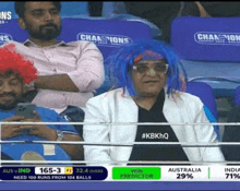 a man wearing a blue wig sits in the stands watching a cricket game