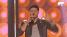 a man in a leather jacket is singing into a microphone while dancing on a stage .