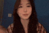 a woman in a plaid shirt looks at the camera with a blue wall in the background