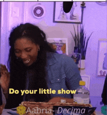 a woman sitting at a table with a bottle of water and a sign that says do your little show