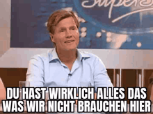 a man in a blue shirt is sitting in front of a sign that says du hast wirklich alles das was wir nicht brachen hier