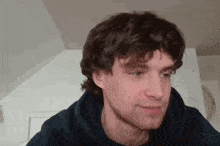 a young man with curly hair and a beard is wearing a hoodie and looking at the camera .