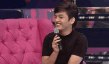 a young man is sitting on a pink couch holding a microphone