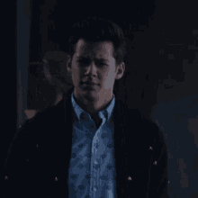 a man wearing a blue shirt and a black jacket looks serious