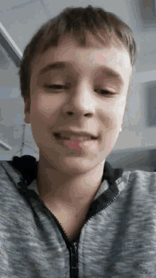 a young boy is making a funny face while wearing a grey jacket .