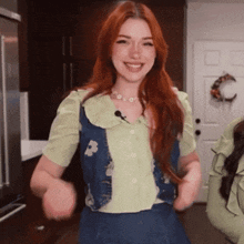 a woman with red hair wearing a green shirt and a blue vest